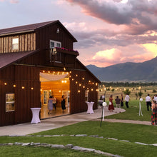 Load image into Gallery viewer, Outdoor event at a barn with mountains in the background and south side bistro lights to illuminate the wedding. 
