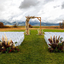 Load image into Gallery viewer, Wooden wedding arch decorated with pampas grass for an outdoor fall wedding at the Rugged Horizon wedding venue in St. Ignatius, Montana. The aisle is marked with large fall centerpieces containing pampas grass, raspberry leaves, and other rich burgundy foliage.
